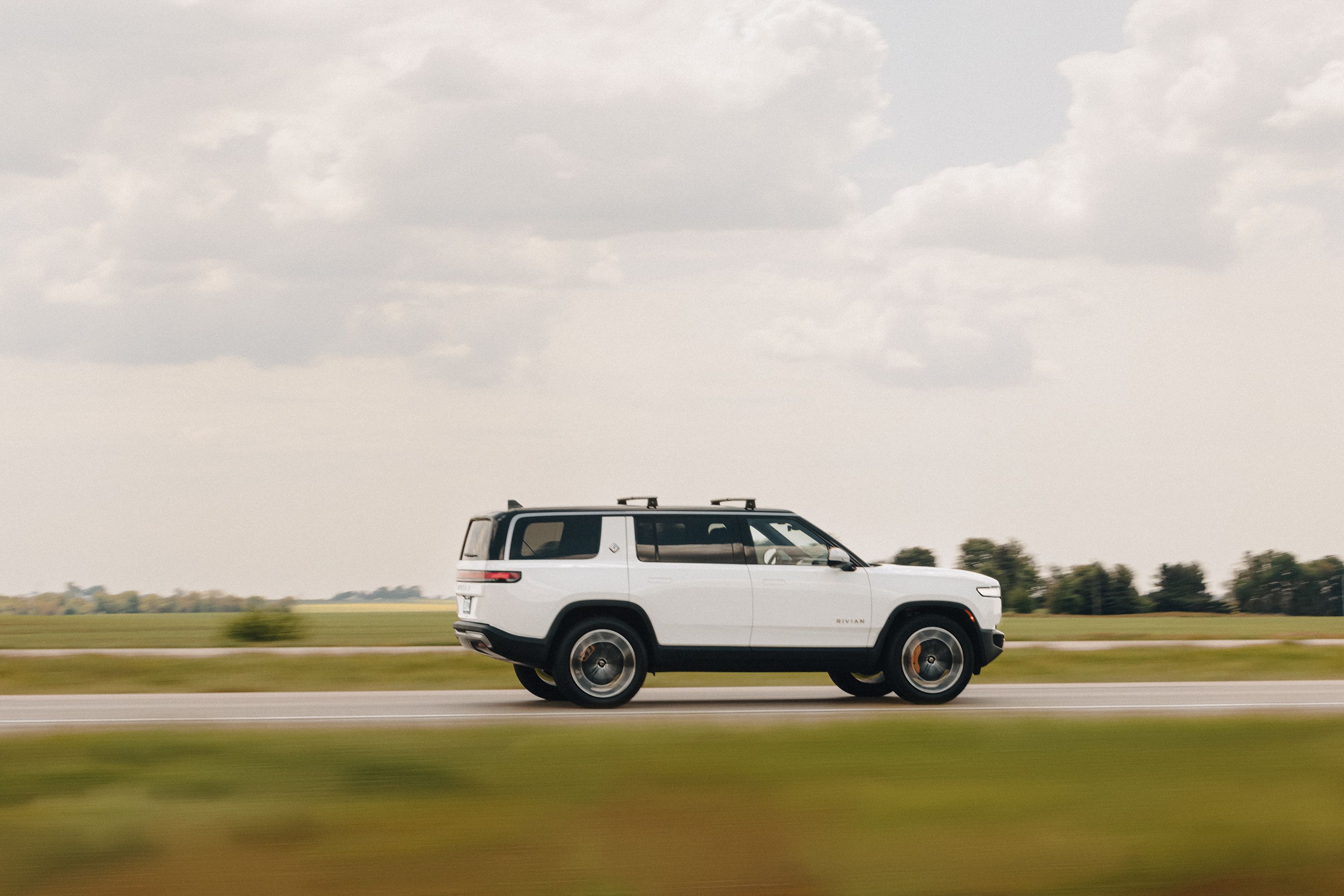 Profile view of a white Rivian R1S SUV on the move.